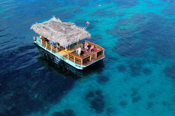 A thatched-roof charter boat anchored on turquoise water at anchor